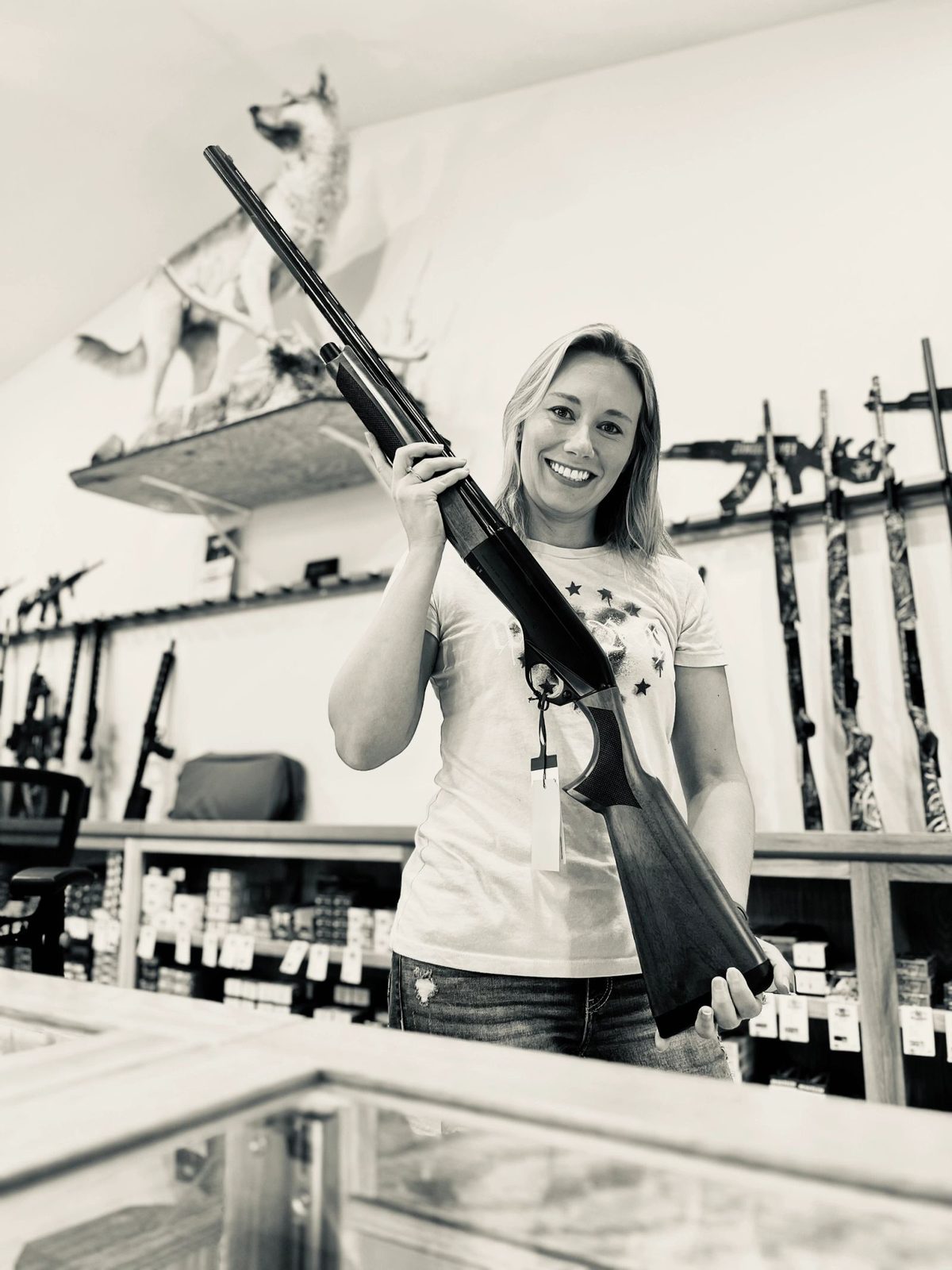 Sabrina presenting a shotgun at the Lady Grey Armament counter, wolf mount overhead